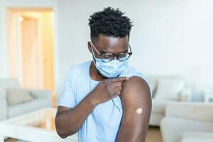 africano hombre participación arriba su camisa manga y demostración su brazo con vendaje después recepción vacunación. codicioso 19 inmunización foto