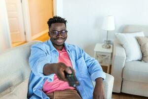 Excited African American Man Pointing Television Controller To Camera Switching Channels Watching TV . Television Programming Advertisement. Selective Focus photo