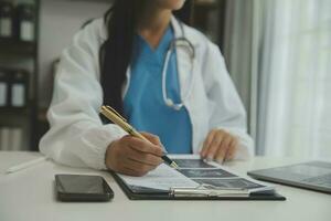 Confident doctor man holding a pill bottle and writing while talking with senior patient and reviewing his medication at office room. photo