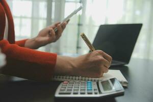 Asian Business woman using calculator and laptop for doing math finance on an office desk, tax, report, accounting, statistics, and analytical research concept photo