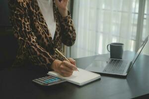 Asian Business woman using calculator and laptop for doing math finance on an office desk, tax, report, accounting, statistics, and analytical research concept photo