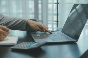 Asian Business woman using calculator and laptop for doing math finance on an office desk, tax, report, accounting, statistics, and analytical research concept photo