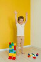 Child raised his hands up while standing on the floor and playing with the wooden multi-colored blocks of the car. Exercise for the brain and coordination of movements. Pre-school employment photo