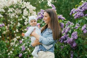 joven madre sostiene su bebé hijo en su brazos en un primavera floreciente lila parque foto