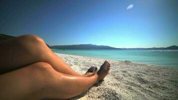 gambe di un' donna prendere il sole nel il sole su il bianca spiaggia nel mare vacanza video