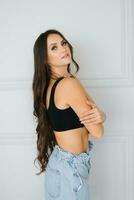 Sensual beautiful young Caucasian woman hugs herself by the shoulders in a black top and jeans photo