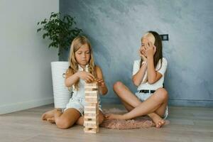 dos hermanas niños con entusiasmo jugar un juego de edificio un torre fuera de de madera bloques a hogar foto