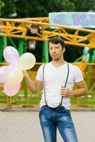 Funny guy is holding a bunch of balloons in his hands at an amusement park waiting for his beloved girl photo