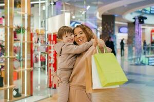 contento y satisfecho madre y pequeño chico niño con compras pantalones en el almacenar. Vamos compras con el niños. foto