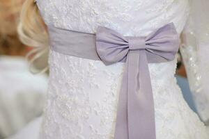 Lilac belt with a bow at the waist of the bride's dress close-up photo