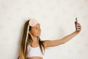 Lovely teenage girl takes a selfie with her smartphone while sitting on the bed after sleeping in the morning photo