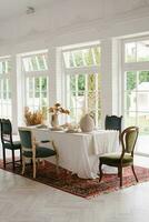 Table set for Thanksgiving with vintage chairs of different shapes and colors in a bright living room with French windows photo