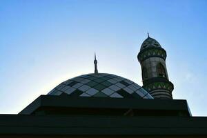 Ornamental dome of the mosque with minaret against blue sky photo