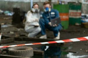 emergency pollution factory concept. engineers wearing mechanic jumpsuits and ppe and gas masks inspect oil on the factory floor. photo