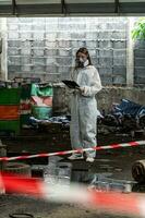 emergency pollution factory concept. Female chemist wearing PPE and gas mask inspecting oil on factory floor photo