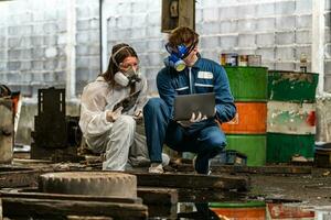 emergency pollution factory concept. engineers wearing mechanic jumpsuits and ppe and gas masks inspect oil on the factory floor. photo