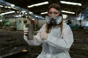 emergencia contaminación fábrica concepto. hembra químico vistiendo ppe y gas máscara inspeccionando petróleo en fábrica piso foto