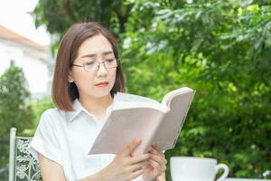 Asian middle aged woman in glasses reading a book in backyard photo