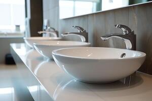 Modern public bathroom with row of white ceramic wash sink basins and faucet with mirror in restroom concept by photo