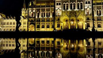 natt skott av budapest parlament byggnad med vatten reflexion och silhuett av turister tar foton video