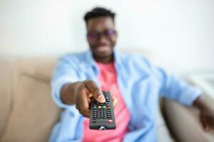 Excited African American Man Pointing Television Controller To Camera Switching Channels Watching TV . Television Programming Advertisement. Selective Focus photo