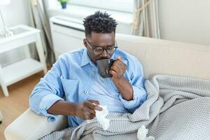 Portrait of a sick man with the flu, allergy, germs,cold coughing. Sick Man with drinking tea sitting under the blanket with high fever and a flu, resting and drinking hot beverage photo