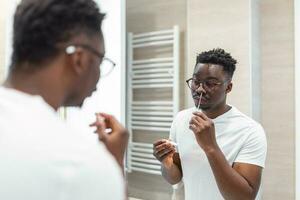 African man doing self test for COVID-19 at home with Antigen test kit. Coronavirus nasal swab test for infection. photo