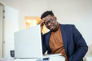 Stressed tired African American man touching temples, suffering from headache after long hours work, overworked overwhelmed businessman sitting at desk, feeling unwell photo