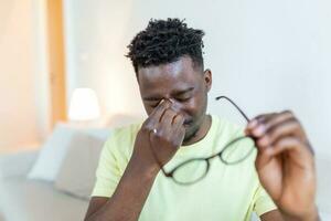African man in glasses rubs his eyes, suffering from tired eyes, ocular diseases concept photo