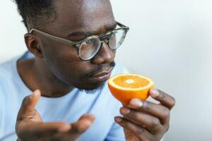 Sick Arican man trying to sense smell of half fresh orange, has symptoms of Covid-19, corona virus infection - loss of smell and taste. One of the main signs of the disease. photo