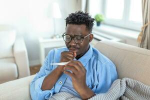Sickness, seasonal virus problem concept. Man being sick having flu lying on bed looking at temperature on thermometer. Sick man lying in bed with high fever. Cold flu coronavirus, covid19 photo