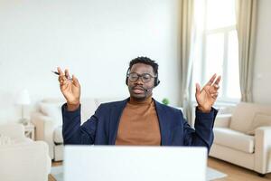 Smiling African American employee in headphones using laptop, looking at screen, making video call or watching webinar, writing notes, distance learning language concept, call center operator working photo