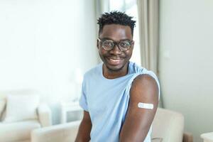 Portrait of a man smiling after getting a vaccine. African man holding down his shirt sleeve and showing his arm with bandage after receiving vaccination. photo