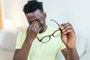 African man in glasses rubs his eyes, suffering from tired eyes, ocular diseases concept photo