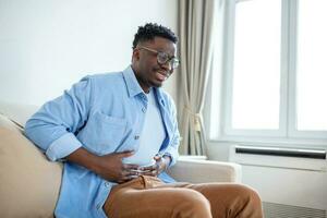 Young African man holding his stomach in pain, Man with reflux disease holding his belly with painful expression photo