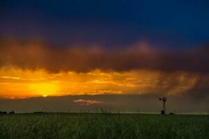 un puesta de sol terminado un campo con un molino en el antecedentes foto