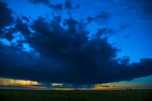 un tormenta nubes terminado un campo a puesta de sol foto