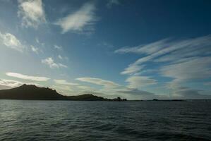 a body of water with a rocky shore and a mountain in the distance photo