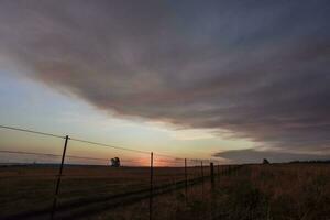 a sunset over a field with a fence and a fence post photo