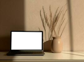 Table with vase and empty screen laptop on wallpaper photo