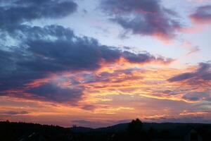 Twilight sky after sunset, clouds in red, orange ,blue, violet, purple, crimson colors. Silhouettes of houses roofs, trees, monastery on the hill and forest. Colorful scenery skyline background. photo