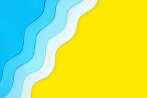 Seaside diagonal background made of color paper. Paper cut blue waves and yellow beach sand with copy space. Summer holidays concept. Relaxation and fun on sea vacations. The ocean coast layout. photo