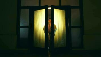 un asiático hombre camina y abre el puerta de un casa equipado con amarillo luces video