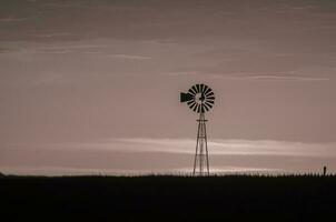 a windmill stands in the middle of a field photo