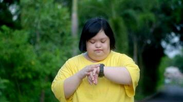 asiatico ragazza con giù sindrome Guarda a il orologio e rallegrati mentre esercizio nel il parco video