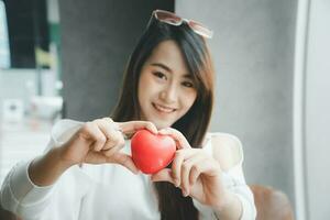 Portrait of beautiful happy Asian woman smiling and holding a red heart. Concept of love and relationship. photo