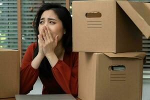 Sad Asian woman Packing belongings in a cardboard box and crying on the desk in the office After being layoff and unemployed. Concept of impact on the economic downturn And management of the failure photo