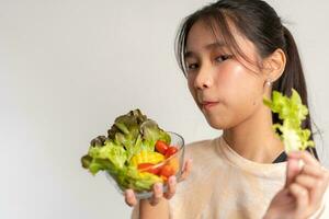 Portrait of a happy playful Asian girl eating fresh salad from a glass bowl after workout at home. Young lady Enjoying Healthy Nutrition And Organic Food, Having Vegetarian Meal photo