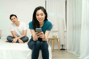 Asian husband feeling suspicious of my wife's abnormality in smartphone use and his wife ignores him and uses the smartphone all time. Concept of relationship problem and Infidelity photo