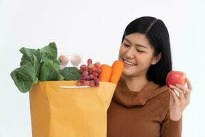 Happy Asian woman is smiling hold apple and carries a shopping paper bag after the courier from the grocery came to deliver his goods at home. Concept of Supermarket delivery for a new lifestyle photo